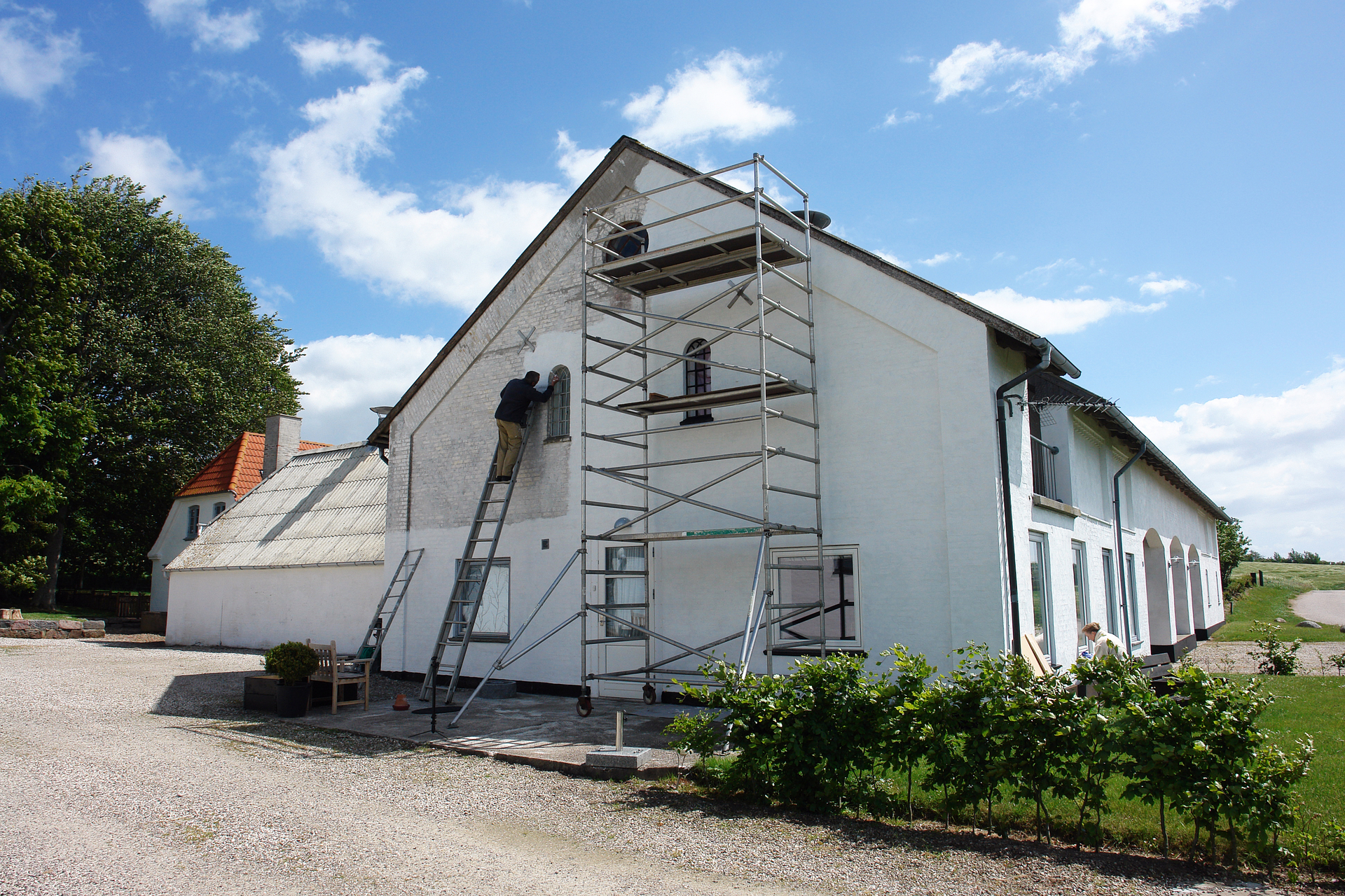 utomhusmålare som står på ställning på gaveln av ett hus